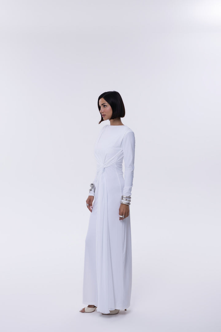 Woman wearing a white long-sleeve top and white pants on a light gray background