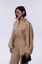 Woman wearing a beige outfit with sunglasses and a black clutch against a white background