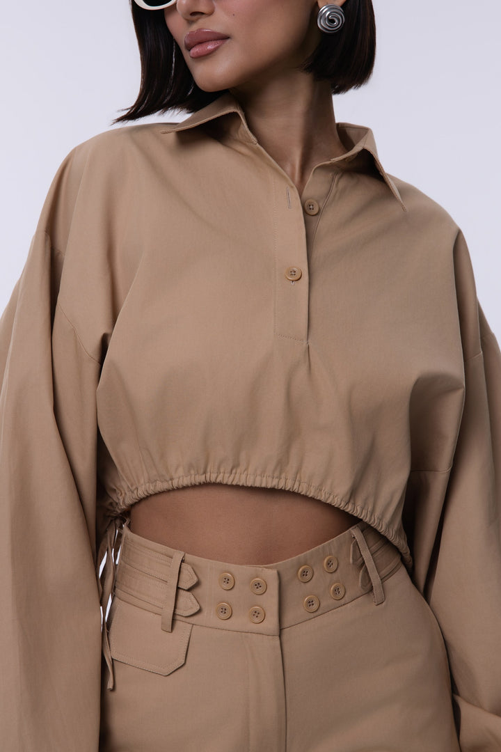 Person wearing a beige cropped shirt and pants set against a white background
