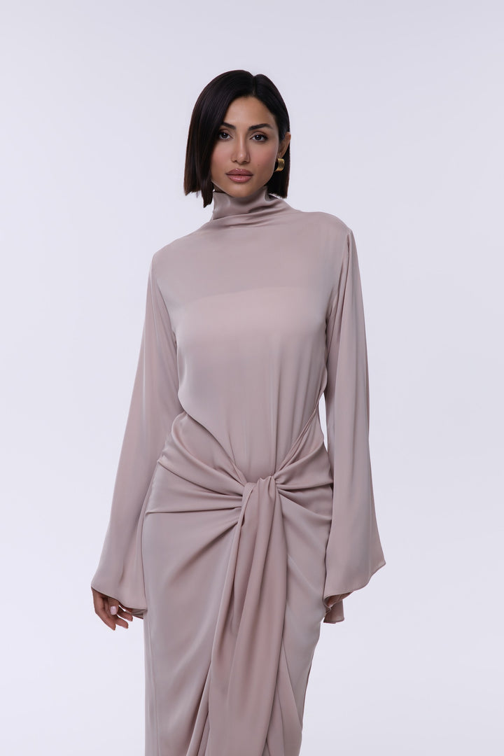 Woman wearing a long beige dress with a knot detail on a white background