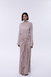Woman wearing a long, light brown dress with a high neckline on a white background