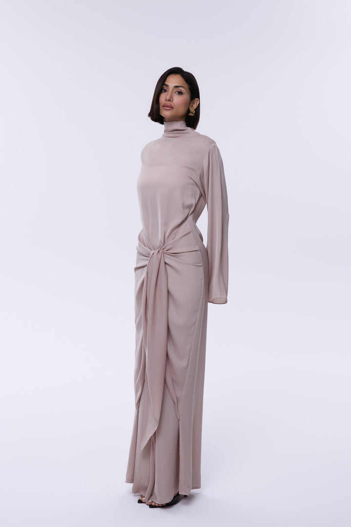Woman wearing a long, light brown dress with a turtleneck on a white background