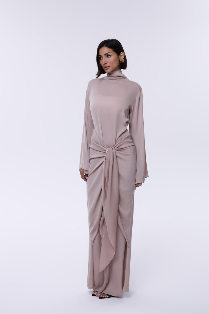 Woman wearing a long, light brown dress with a knot detail on a white background