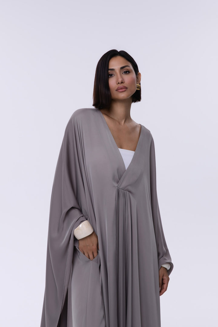 Woman wearing a gray abaya over a white top on a light gray background