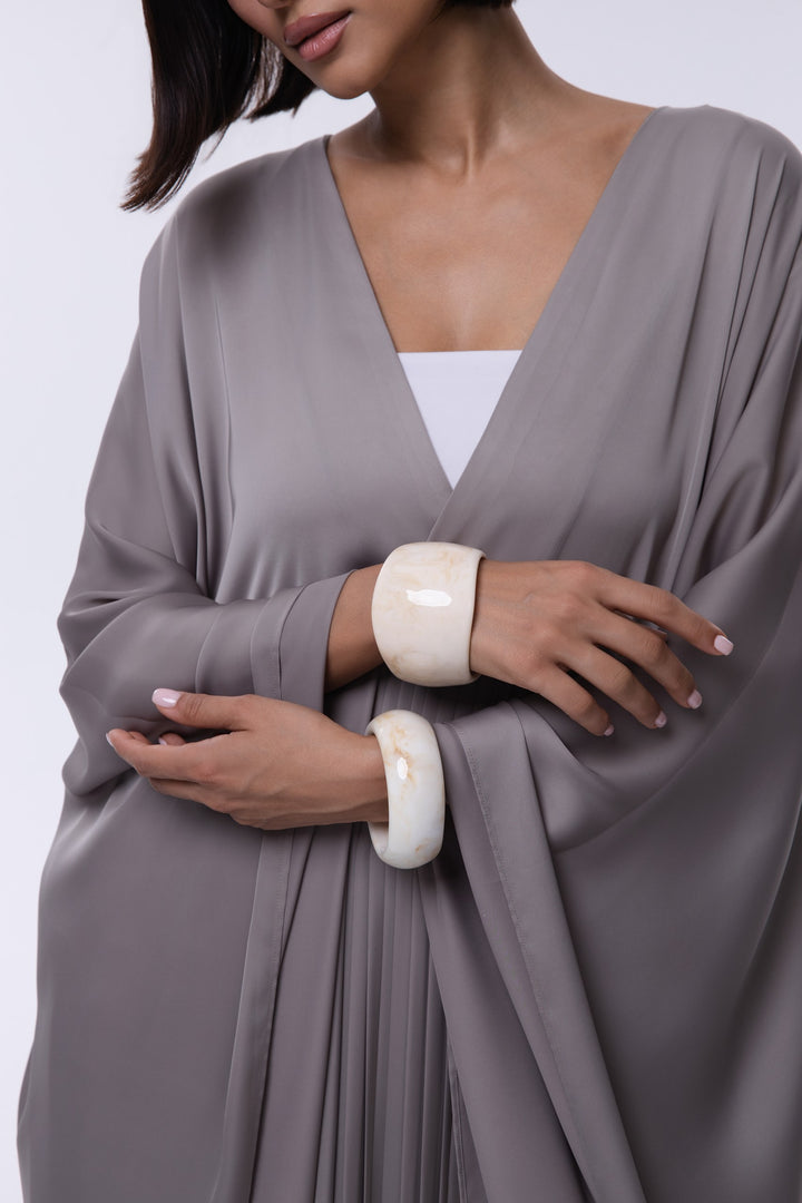 Woman wearing a gray draped garment with white cuffs on a plain background