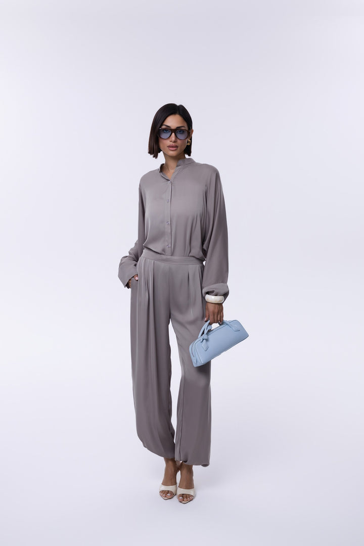 Woman in gray outfit holding a blue clutch against a white background