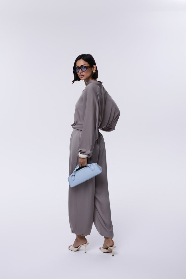 Woman in a gray outfit holding a blue clutch against a white background