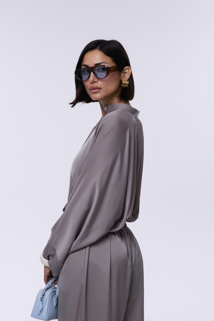 Woman wearing a gray outfit with sunglasses and a light blue handbag on a white background