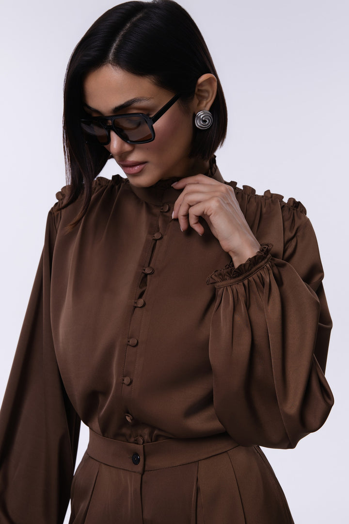 Woman wearing a brown blouse with long sleeves and buttons on a white background