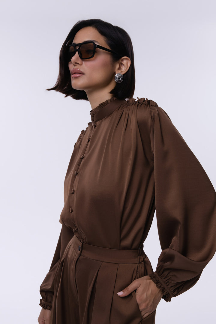 Woman wearing a brown long-sleeve top with a high collar against a white background