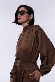 Woman wearing a brown long-sleeve top with a high collar against a white background