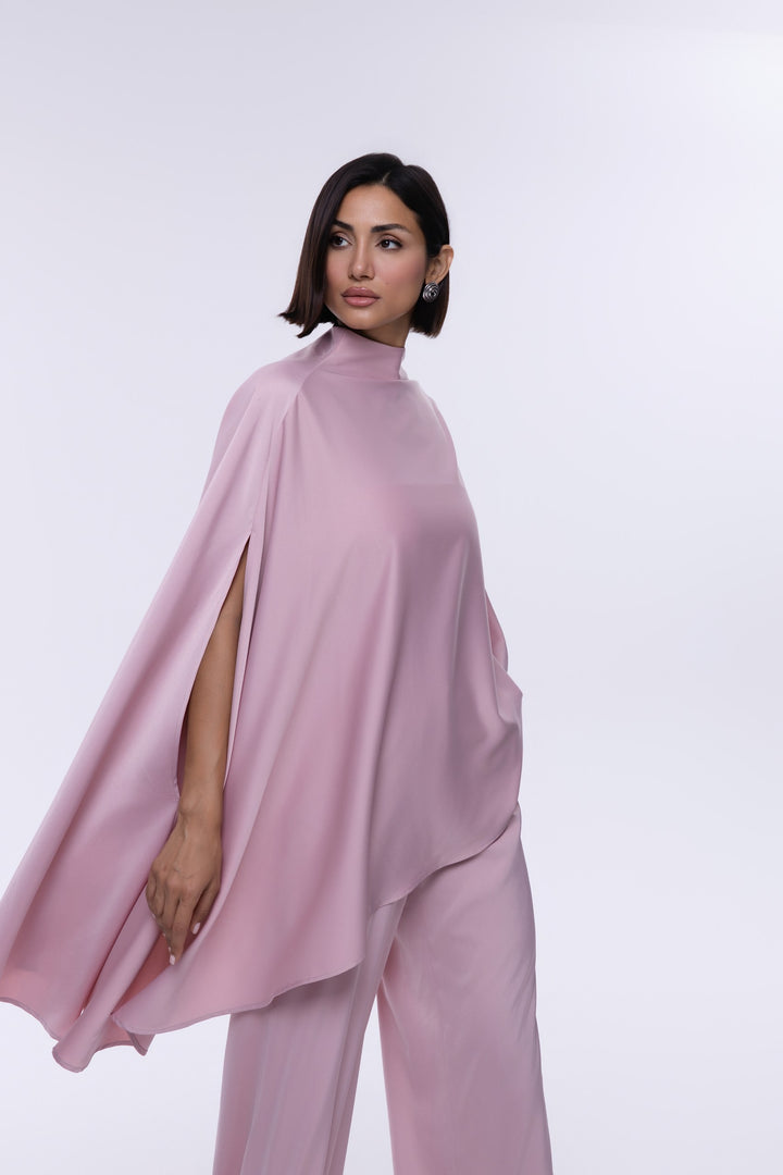 Woman wearing a pink cape and pants on a white background