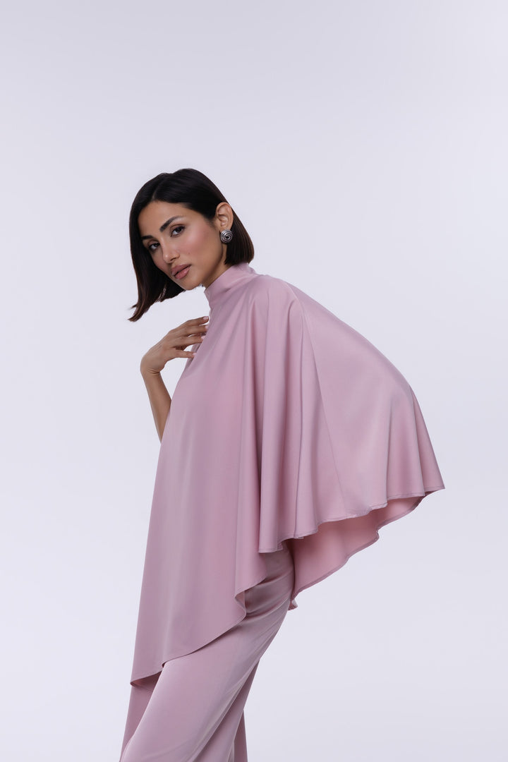 Woman wearing a pink outfit with a cape on a white background