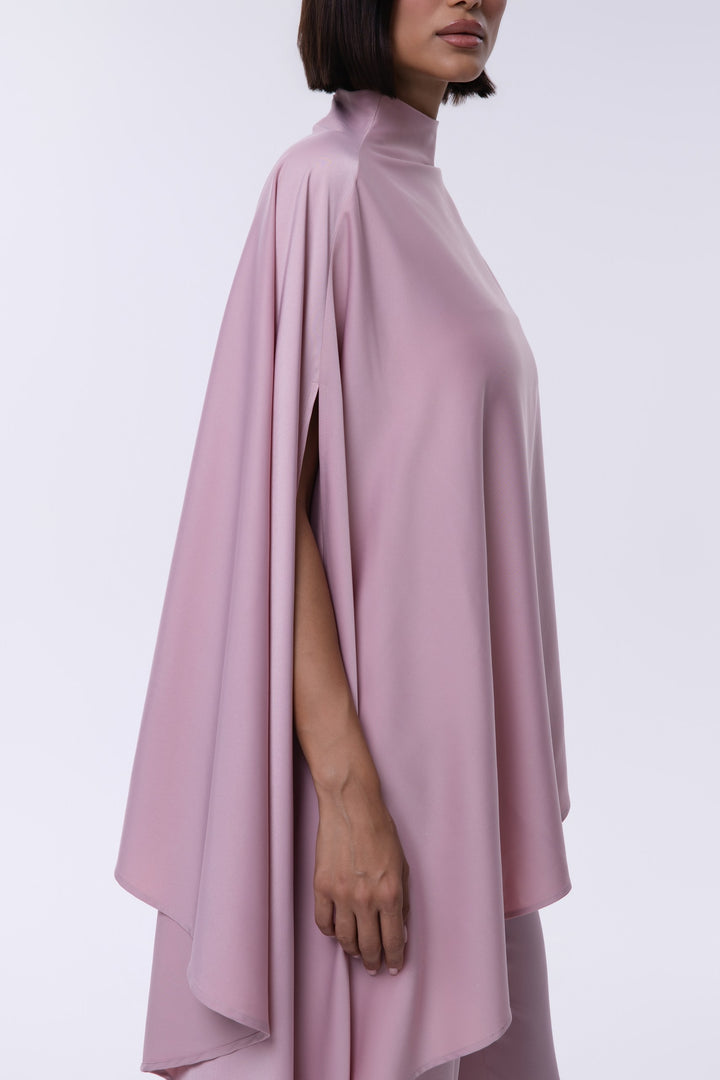 Person wearing a pink cape over a plain background