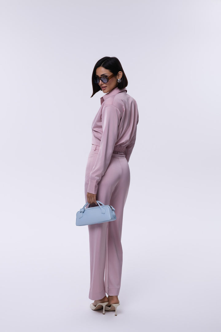Woman in a pink outfit holding a blue handbag against a white background